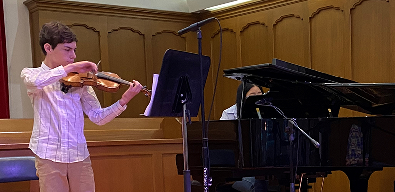 Young man playing violin with woman accompanying him on piano